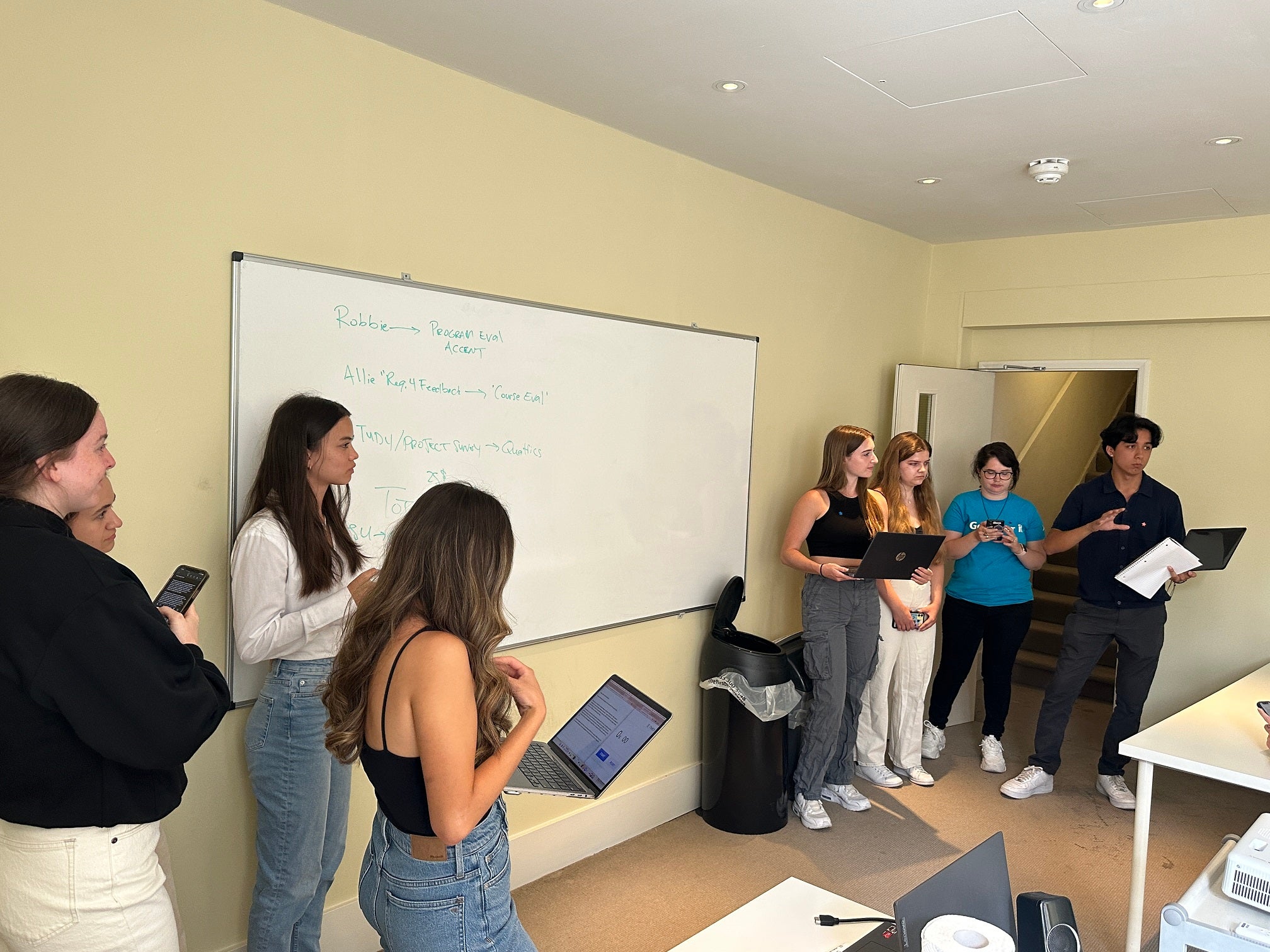 Students stand at the front of a classroom, some with laptops in their hands while carrying out an in-class debate assignment.