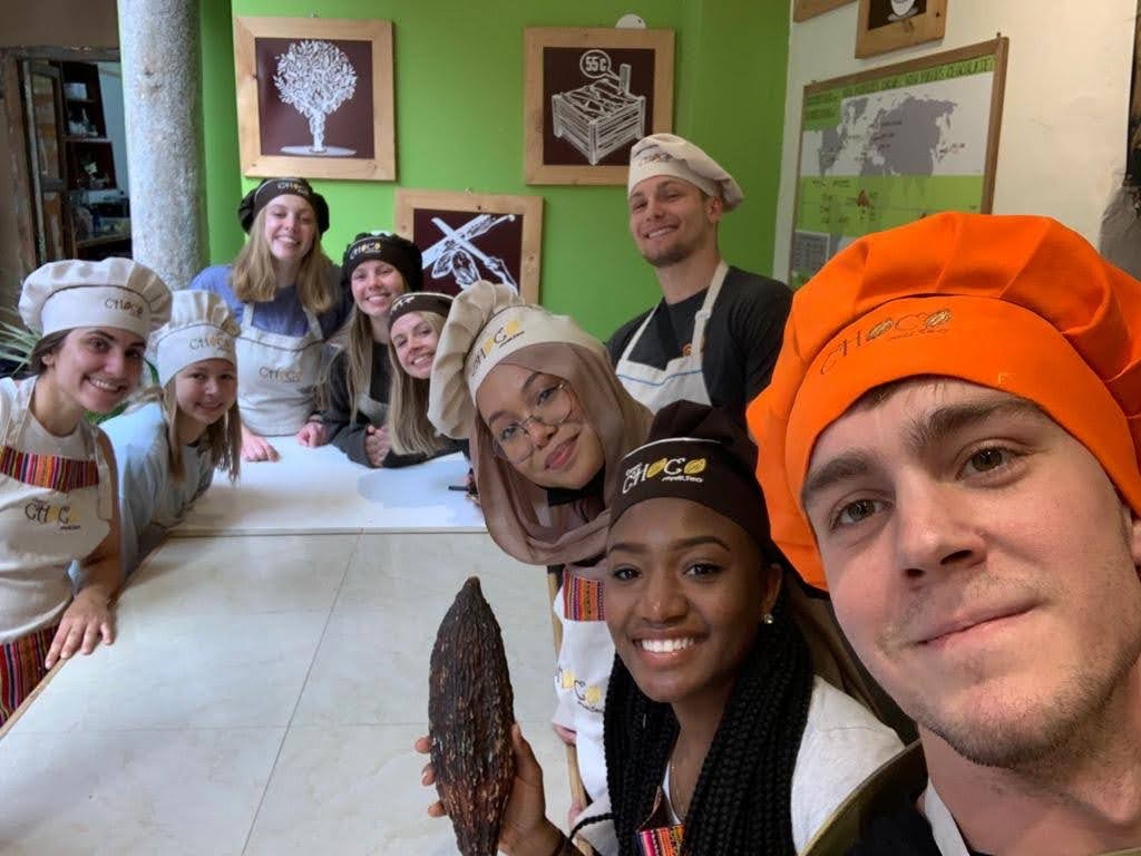 Students wear aprons and chefs hats to pose for a photo in a kitchen