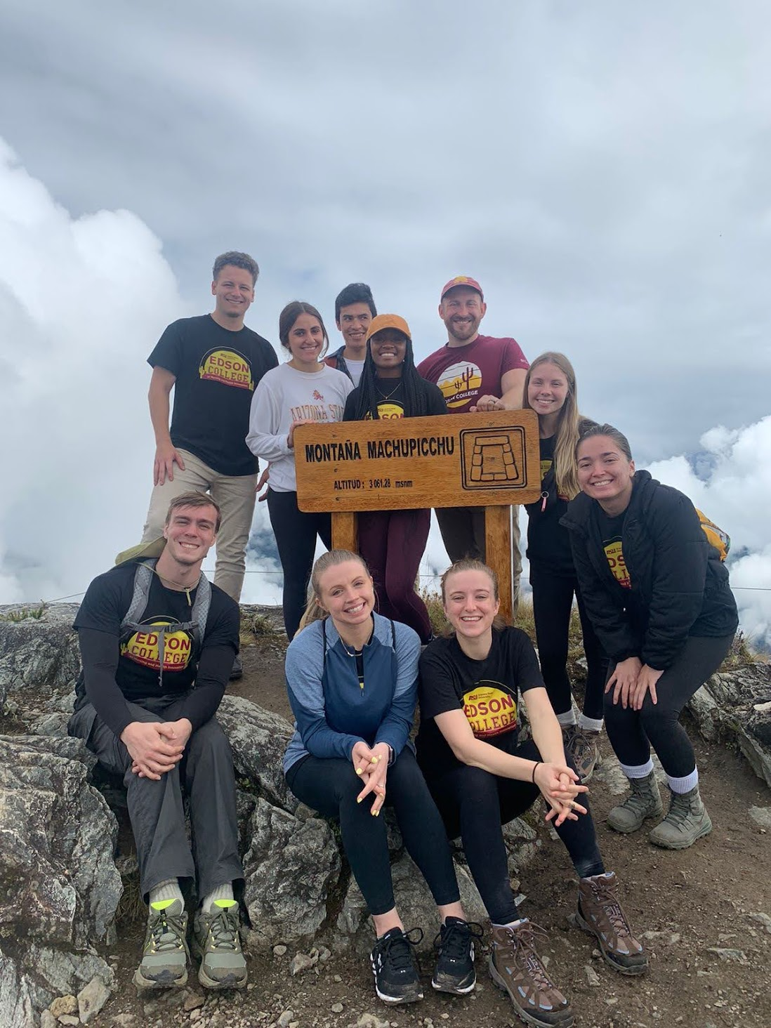 Students in hiking gear pose for a photo with the Machu Picchu sign