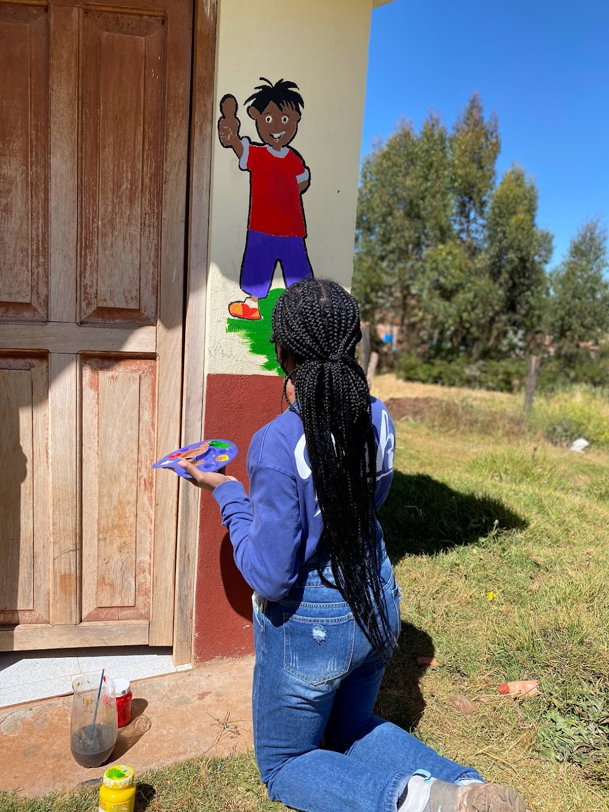 ASU student paints part of a mural on a school.