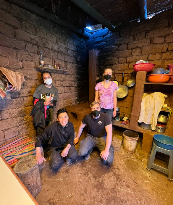 ASU students pose inside a community member's home by a mud stove they just built