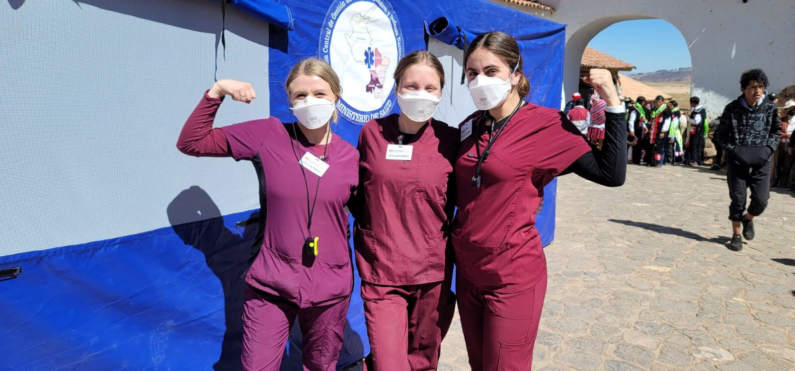 Edson College students pose in maroon scrubs with blue surgical masks on outside of a clinic in Peru