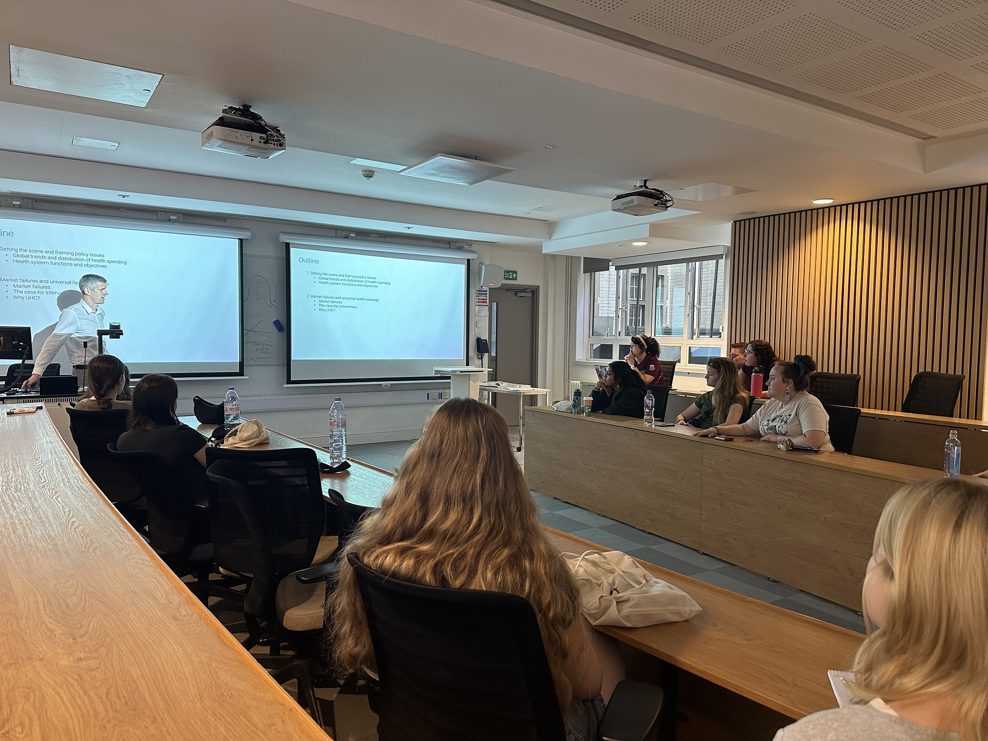 Students sit at desks at the London School of Economics while listening to a presentation by George Wharton