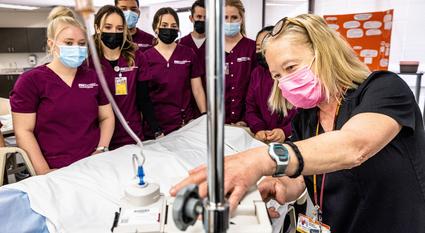 Edson College nursing students watch as an instructor demonstrates something on an IV pump