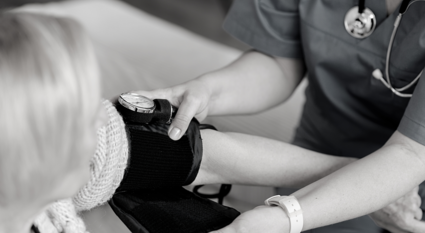 The hands of a nurse are seen putting a blood pressure cuff on a patient. Both faces are not visible only their arms